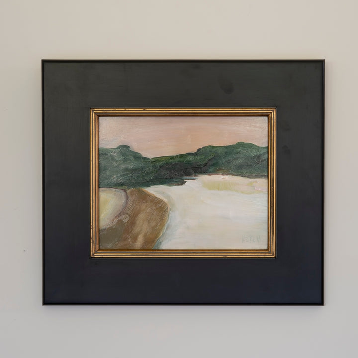 A framed landscape painting featuring green hills, a brown foreground, and a pale sky, mounted with a wide black mat and a thin gold inner frame on a light gray wall.