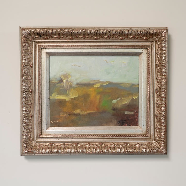 An oil landscape painting in an ornate, carved silver-toned frame, hung on a light neutral wall.